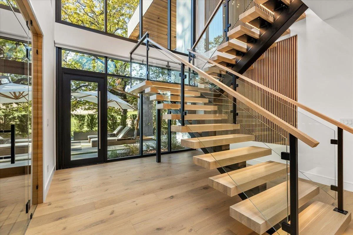 Modern staircase with hardwood treads, glass railings, and black metal supports in bright open home