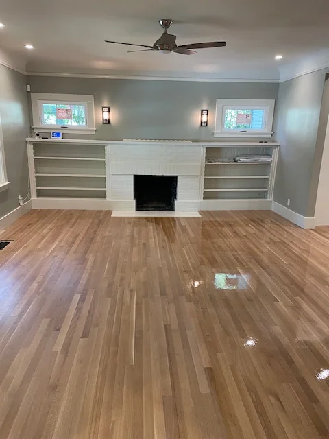 Newly installed hardwood flooring in living room with fireplace and built-in shelving