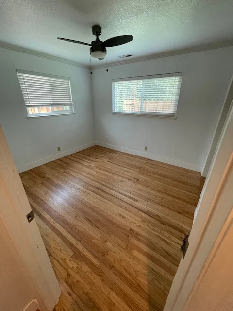 Newly installed laminate flooring in bedroom with white walls and black ceiling fan