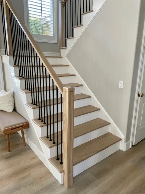Modern staircase with wood treads, white risers, natural wood handrail, and black metal balusters