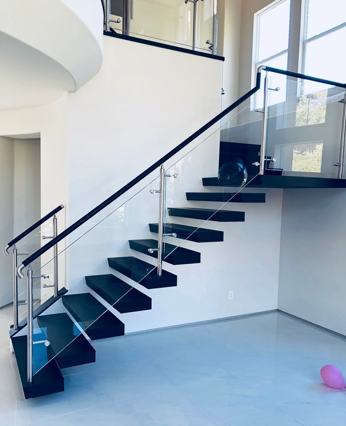 Modern floating staircase with black treads, chrome railings, and glass panels in bright interior