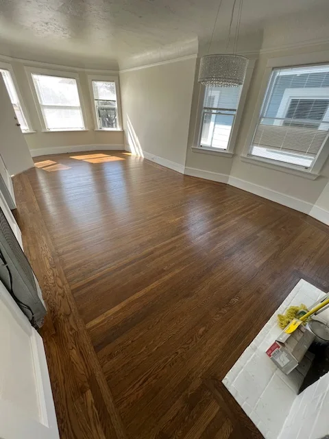 Newly installed medium-tone hardwood flooring in bright living room with bay windows