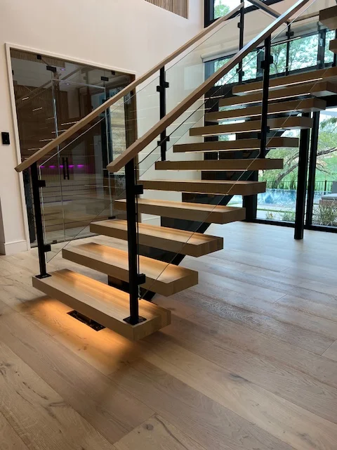 Modern floating staircase with wood steps, black metal railings, and glass panels in contemporary home