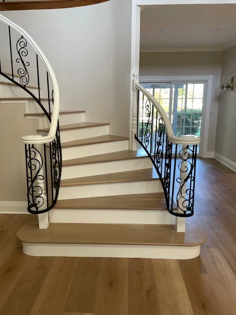 Curved wooden staircase with black iron railings and hardwood flooring in modern home entry