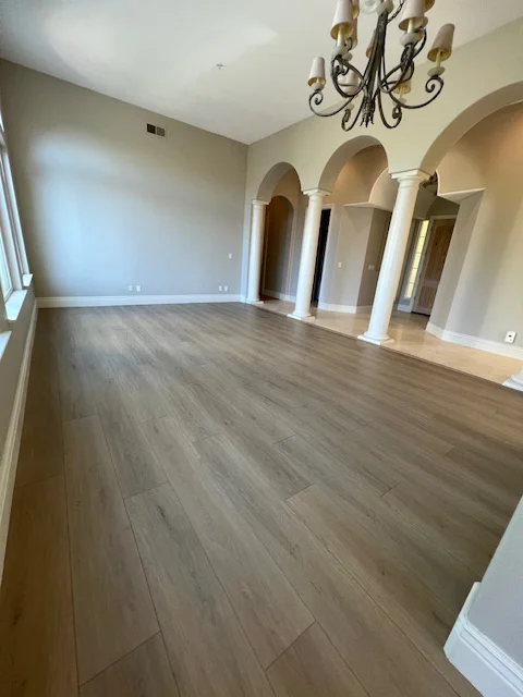 Luxury vinyl plank flooring in spacious room with white columns and arched doorways