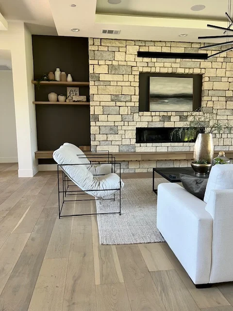 Light wood plank flooring in modern living room with white furniture and stone fireplace
