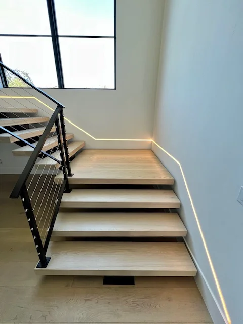 Modern wooden staircase with black metal cable railing and recessed lighting